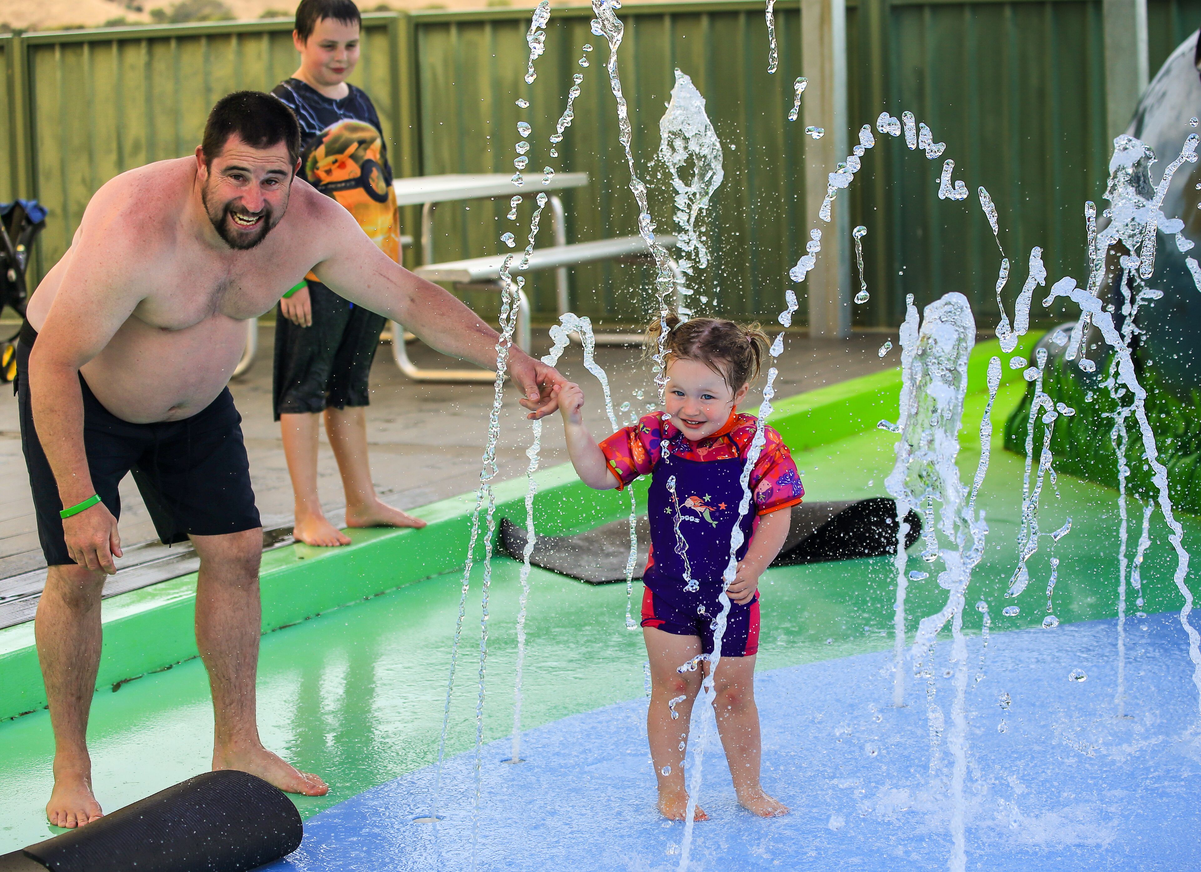 A man and a child playing with water jets at a pool.