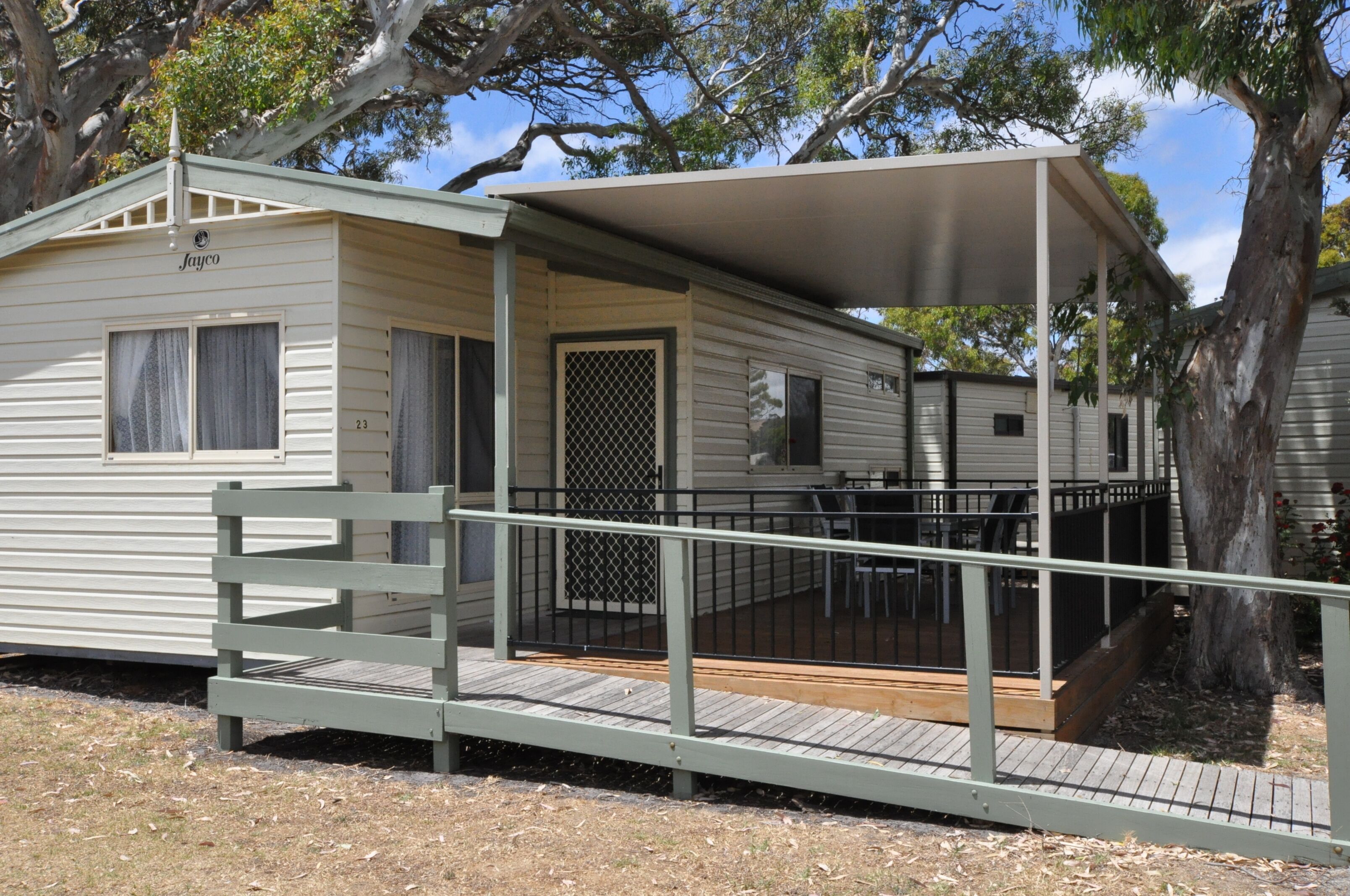 A mobile home with a covered porch and a fenced deck area.