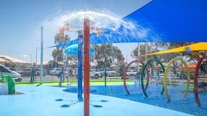 Zona de juegos acuáticos al aire libre con estructuras coloridas y un toldo azul.