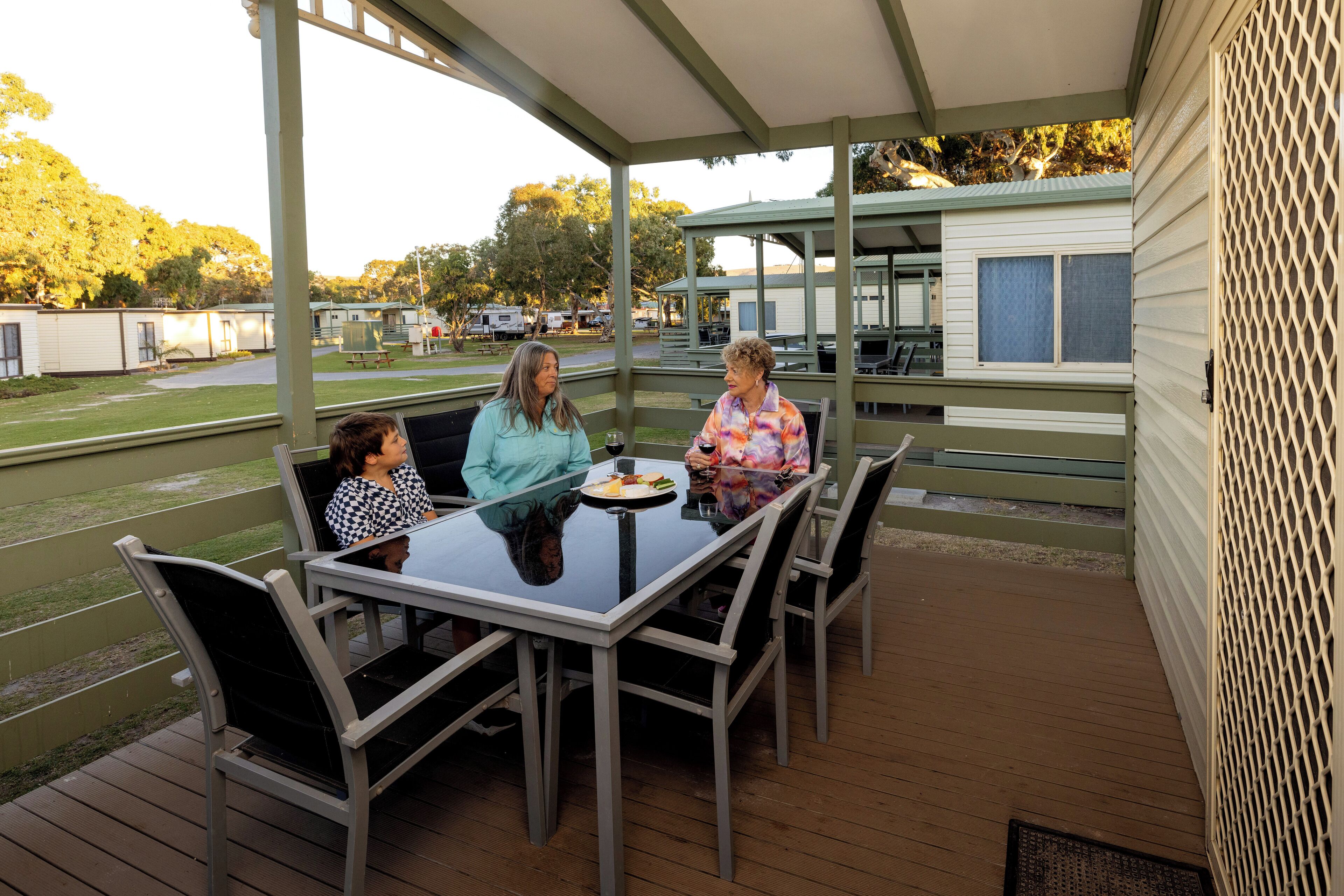 A covered outdoor seating area with a table and chairs, overlooking a campground with mobile homes and trees.