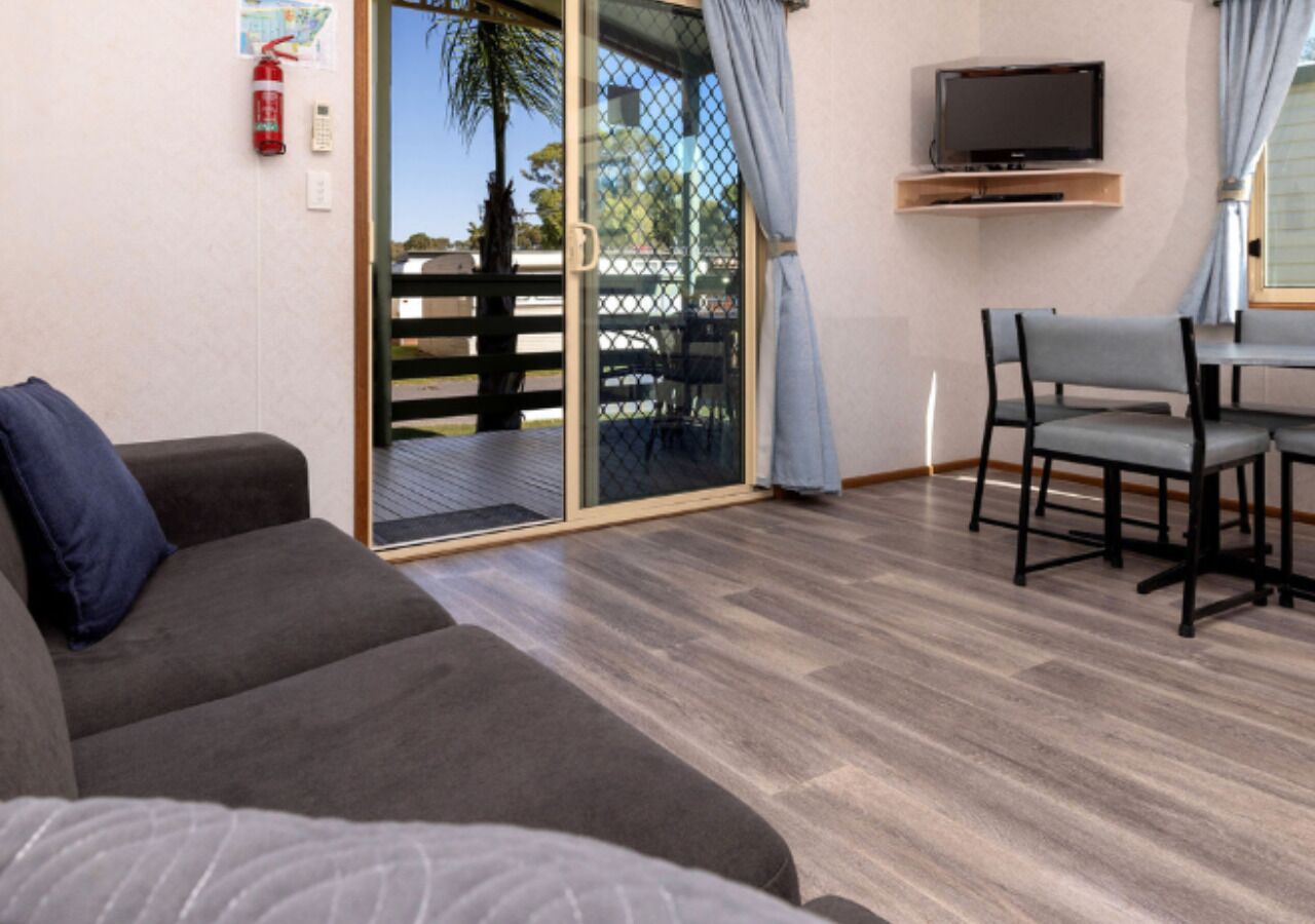Ein Zimmer mit einer Couch, einem Fernseher, einem Esstisch mit Stühlen und einer Glastür zum Außenbereich.