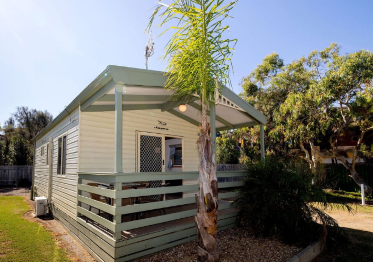 A small, single-story mobile home with a fenced deck, a covered porch, and a small window.