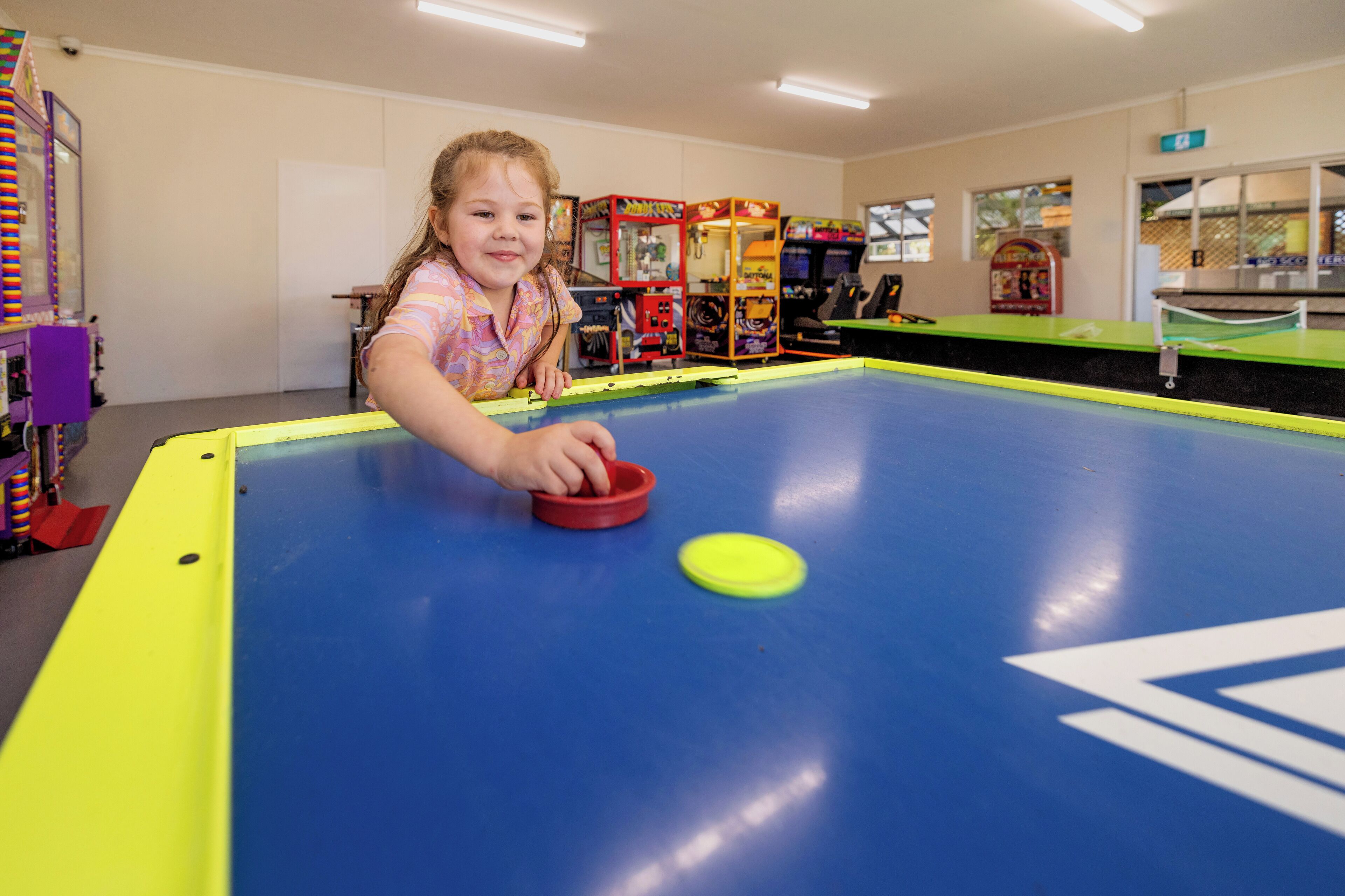 A child playing pool in a room with arcade games in the background.