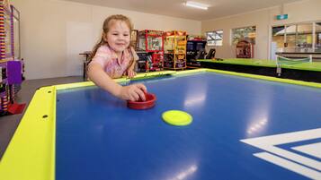 A child playing pool in a room with arcade games in the background.