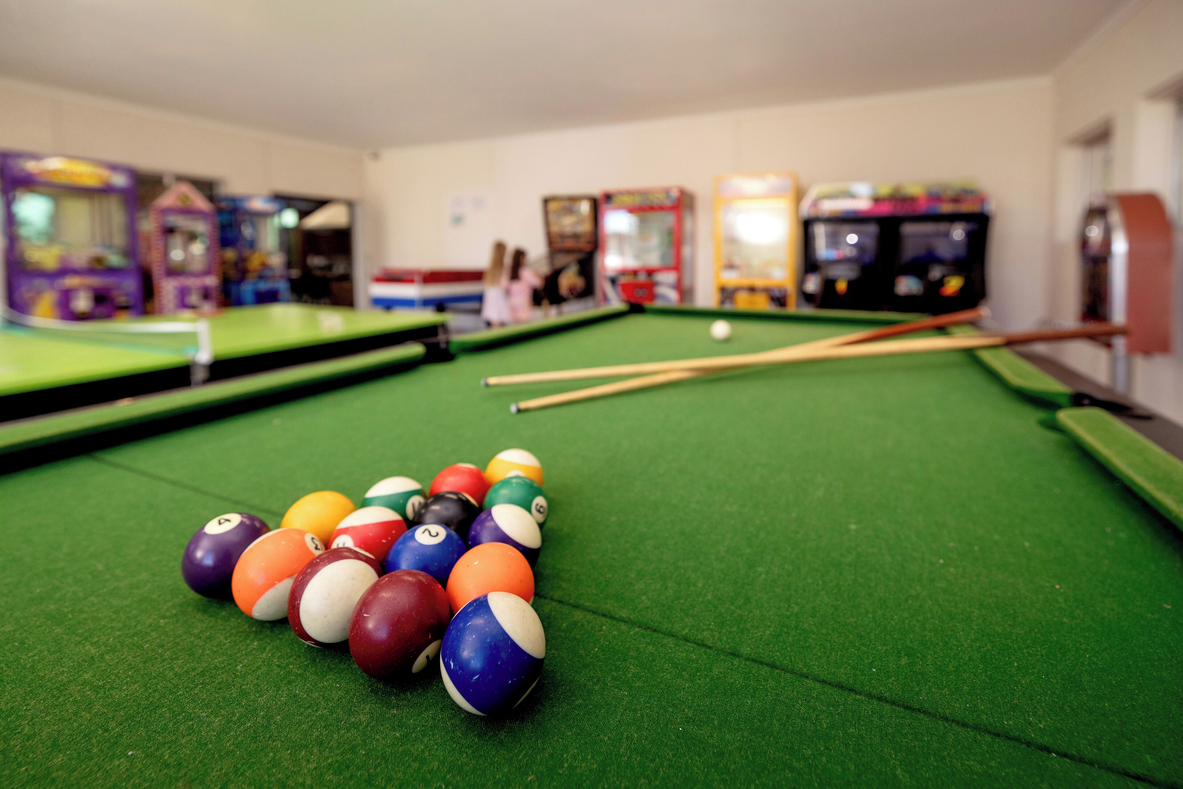 A pool table with balls and cues, surrounded by arcade machines.