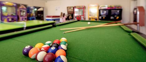 A pool table with balls and cues, surrounded by arcade machines.