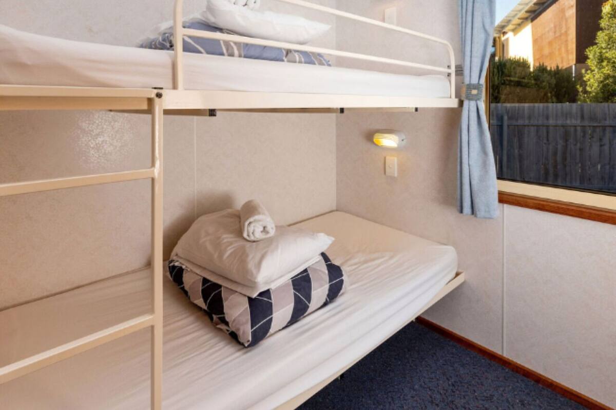 Una cama litera con una cama inferior, una mesita de noche con una lámpara y una ventana con cortinas.