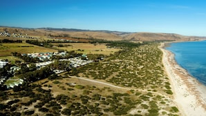 Vista aérea de una zona costera con playa, un pequeño poblado con casas y colinas al fondo.