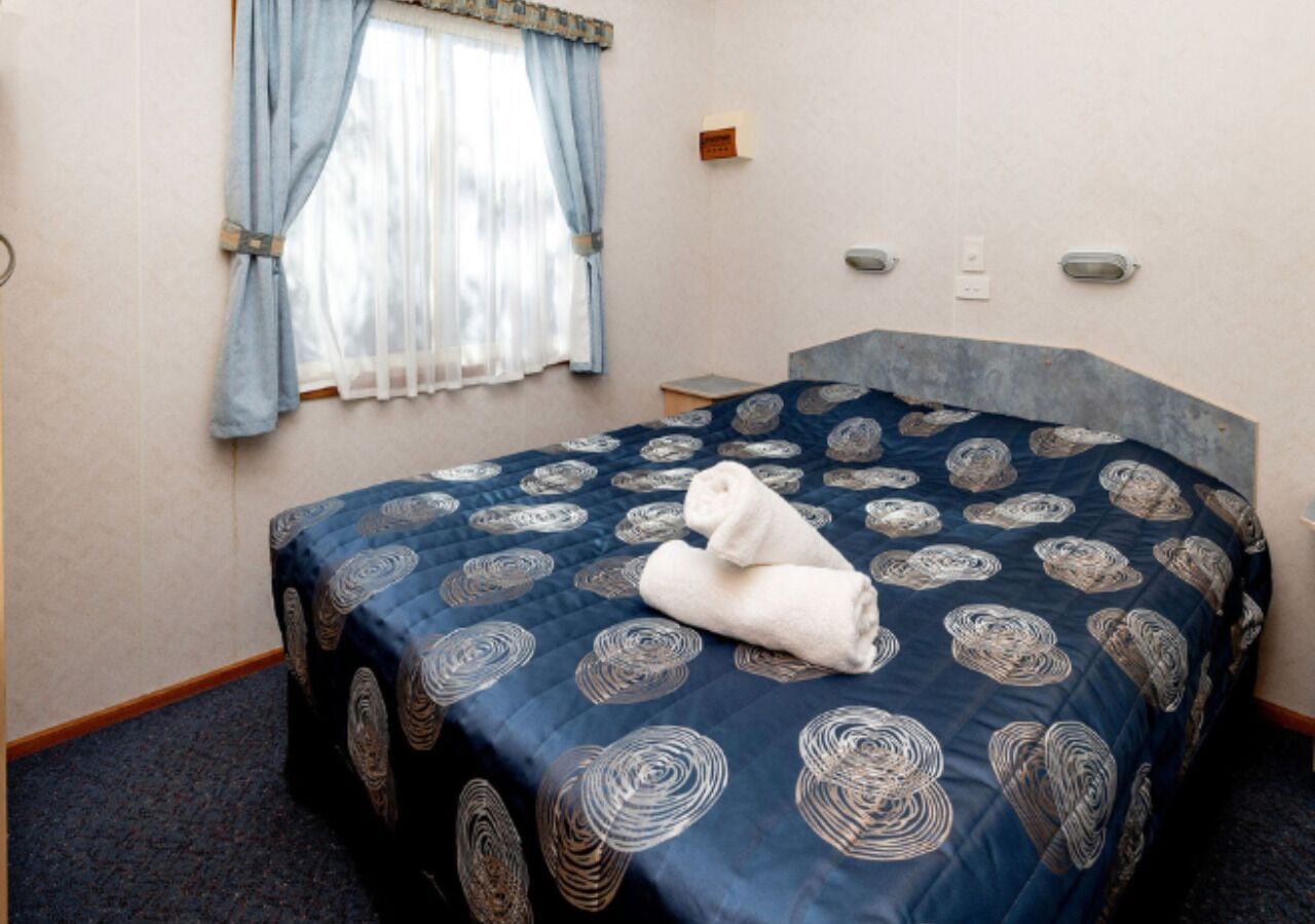 A hotel room with a bed, a window with curtains, a bedside table, and a wall-mounted light.