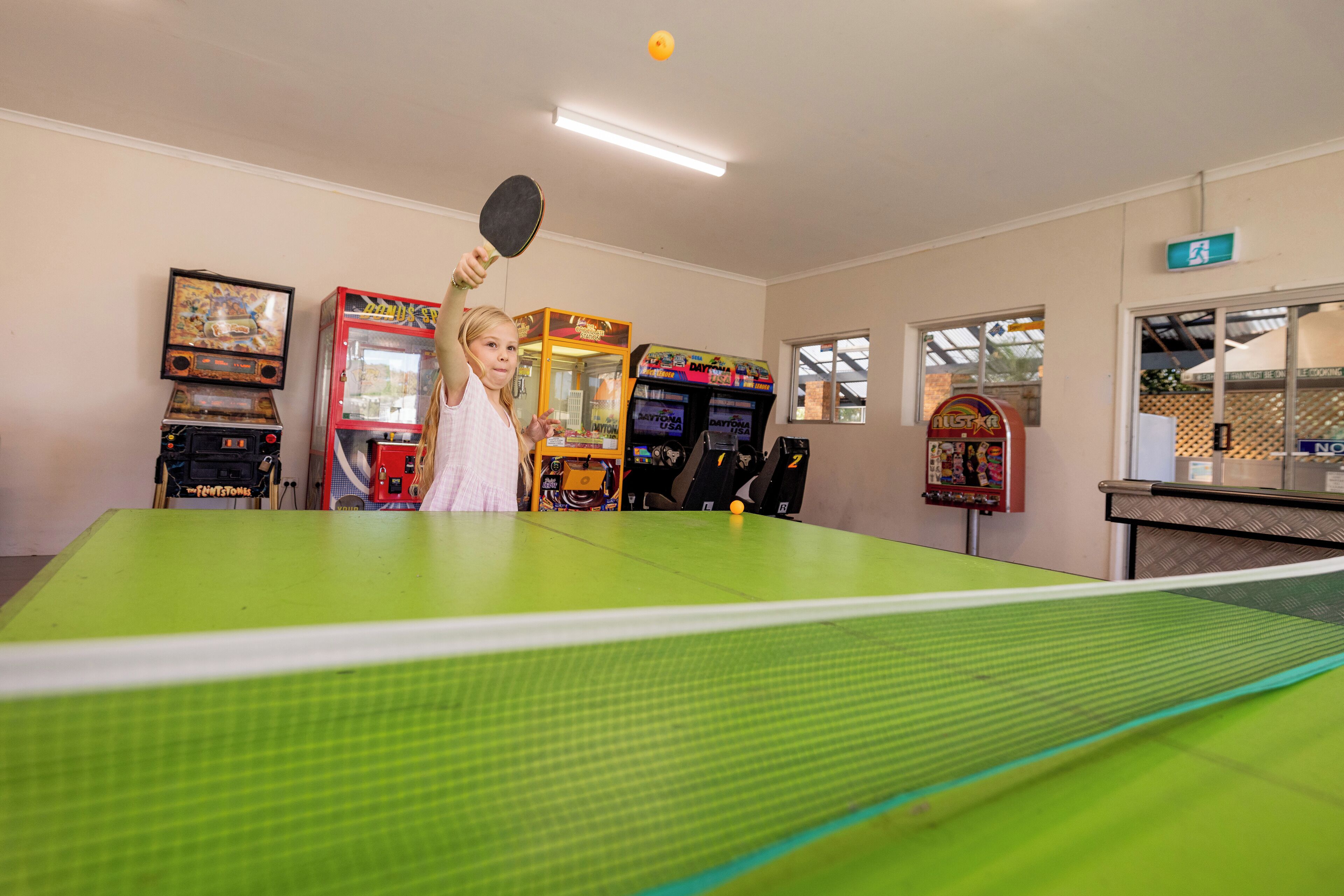 A ping pong table in a room with arcade games and a window.