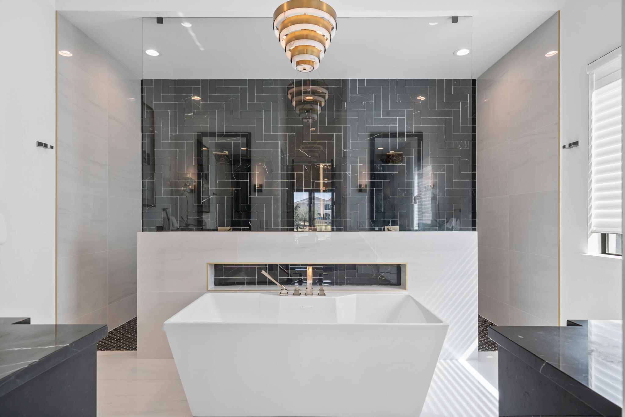 Un baño moderno con una bañera independiente grande, paredes de azulejos oscuros y un espejo amplio sobre el lavabo.