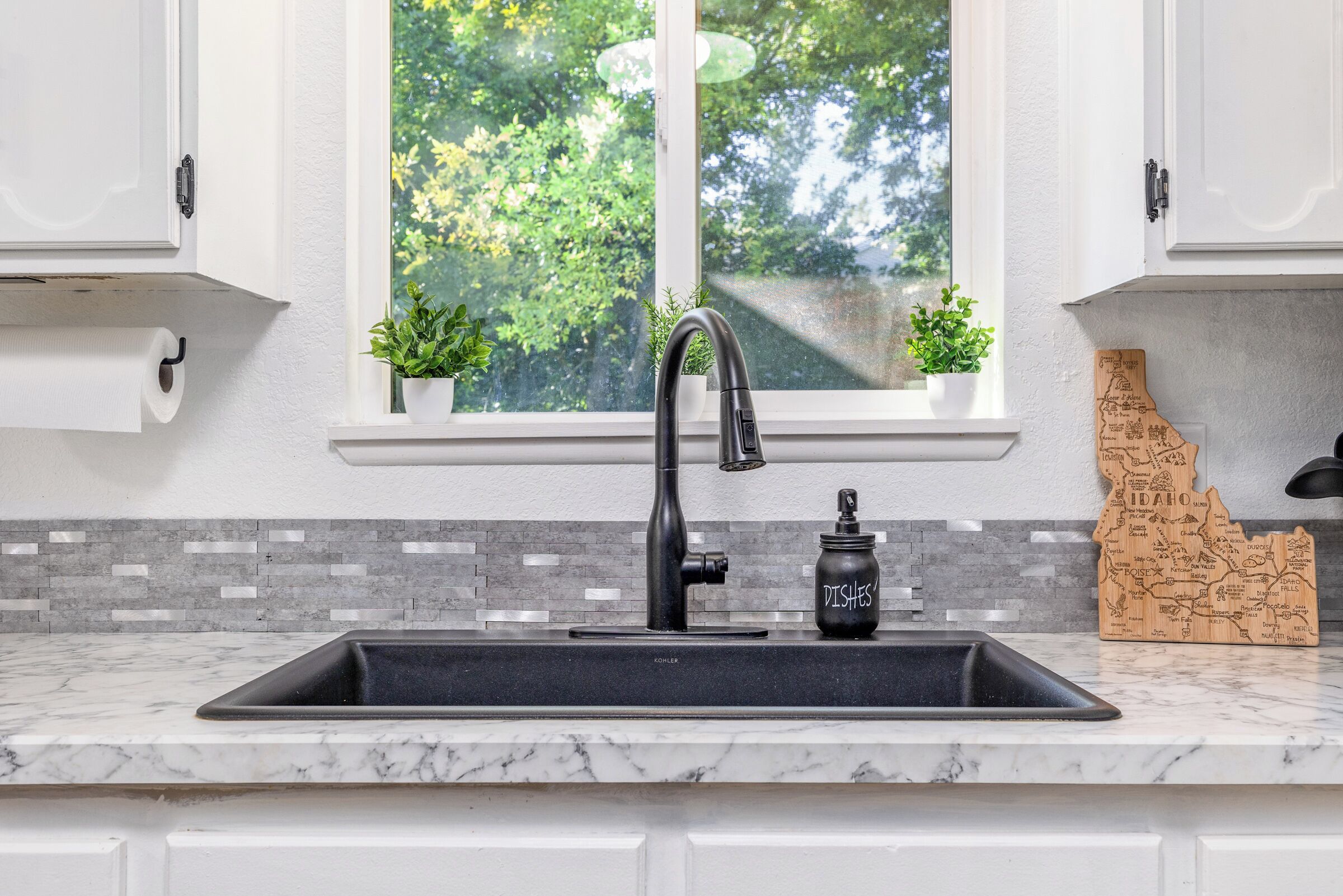 A kitchen with a black faucet, a marble countertop, a window with plants, and a map decoration.
