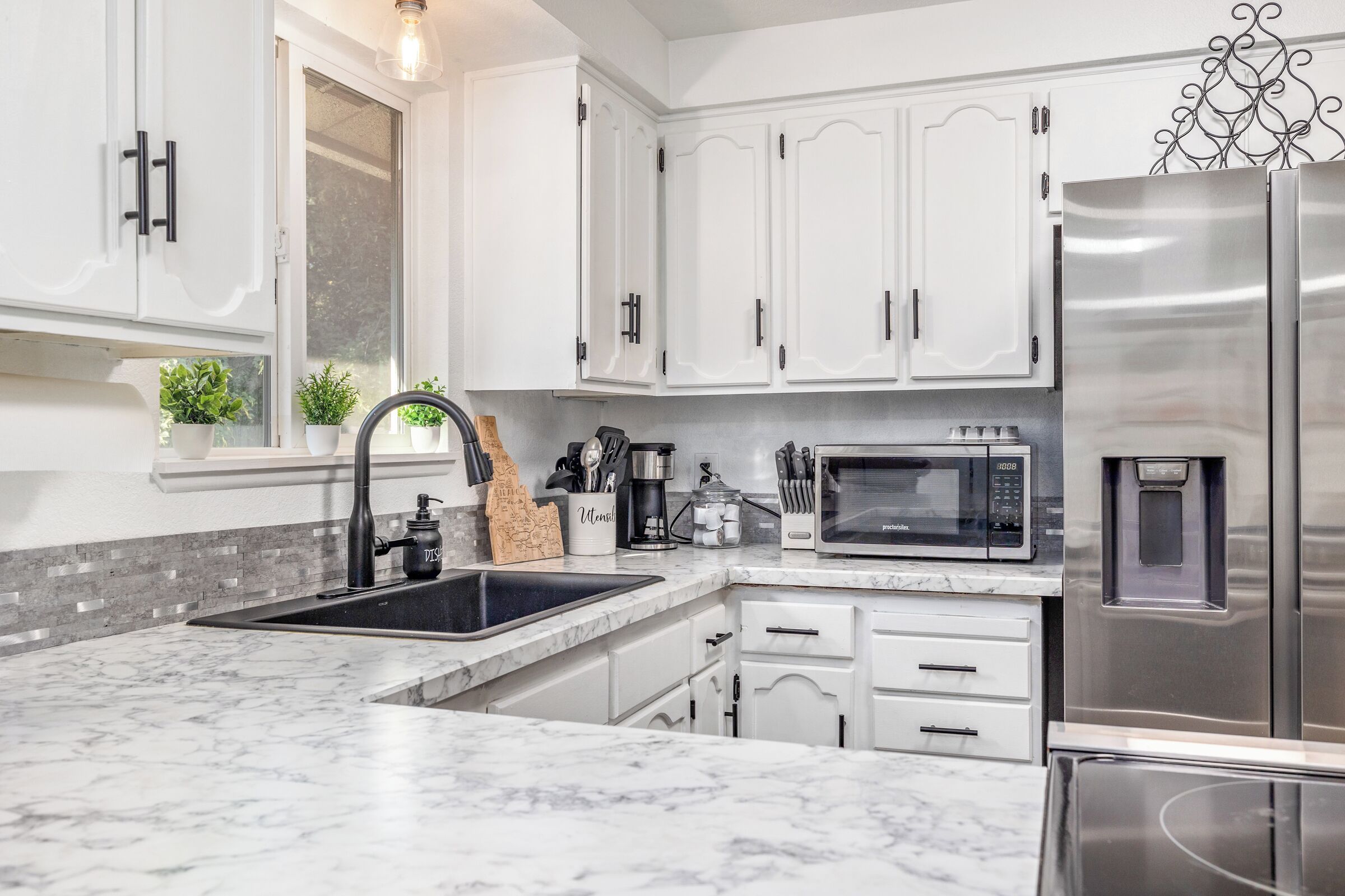 A modern kitchen with white cabinets, a stainless steel refrigerator, a built-in microwave, and a sink with a black faucet.