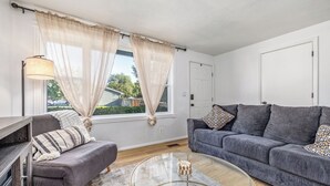 A modern living room with a grey sofa, a glass coffee table, and a TV stand. - Cozy Boise Gem: Private Yard, Game Room & Workspace
 (BOISE)