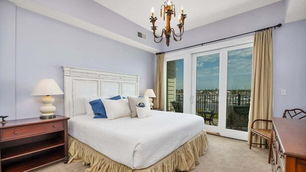 Ein Schlafzimmer mit einem großen Bett, einem Nachttisch, einer Kommode, einer Chandelüster und einem Balkon mit Blick.