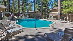 Une piscine entourée de chaises longues et de parasols, bordée de grands arbres et protégée par une clôture.