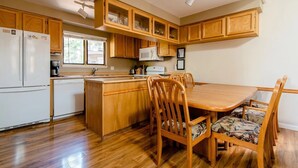 Une cuisine avec des meubles de rangement en bois, un réfrigérateur blanc, un four à micro-ondes et un coin repas comprenant des chaises et une table en bois.