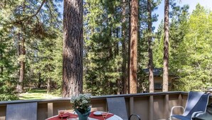 Une terrasse extérieure avec une table ronde dressée pour le repas, entourée de chaises, et donnant sur une zone boisée.