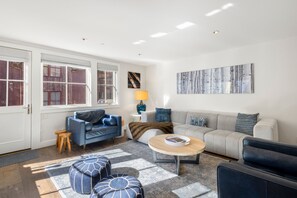 A modern living room with a blue sofa, grey sofa, and a coffee table. There are two windows with curtains, a lamp, and a painting on the wall. - Walk to Ski! Luxury Telluride Townhome | Walk to Gondola, Main Street & River Trail |  | Sleeps 8 (Telluride)