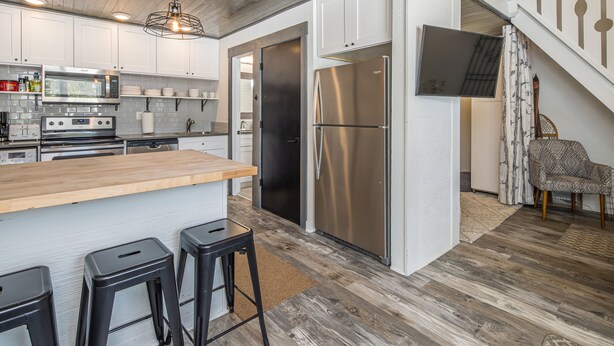 A modern kitchen with stainless steel appliances, a wooden island, and black bar stools.