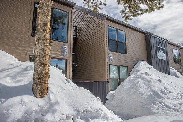 A modern building with multiple windows and a sign indicating unit numbers. Snow is piled in front of the building.
