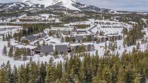 A snow-covered resort with multiple buildings, a ski slope, and a mountain in the background.