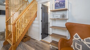 A wooden staircase leading to a dark door, a brown leather chair with a patterned pillow, and a wall with a framed map.
