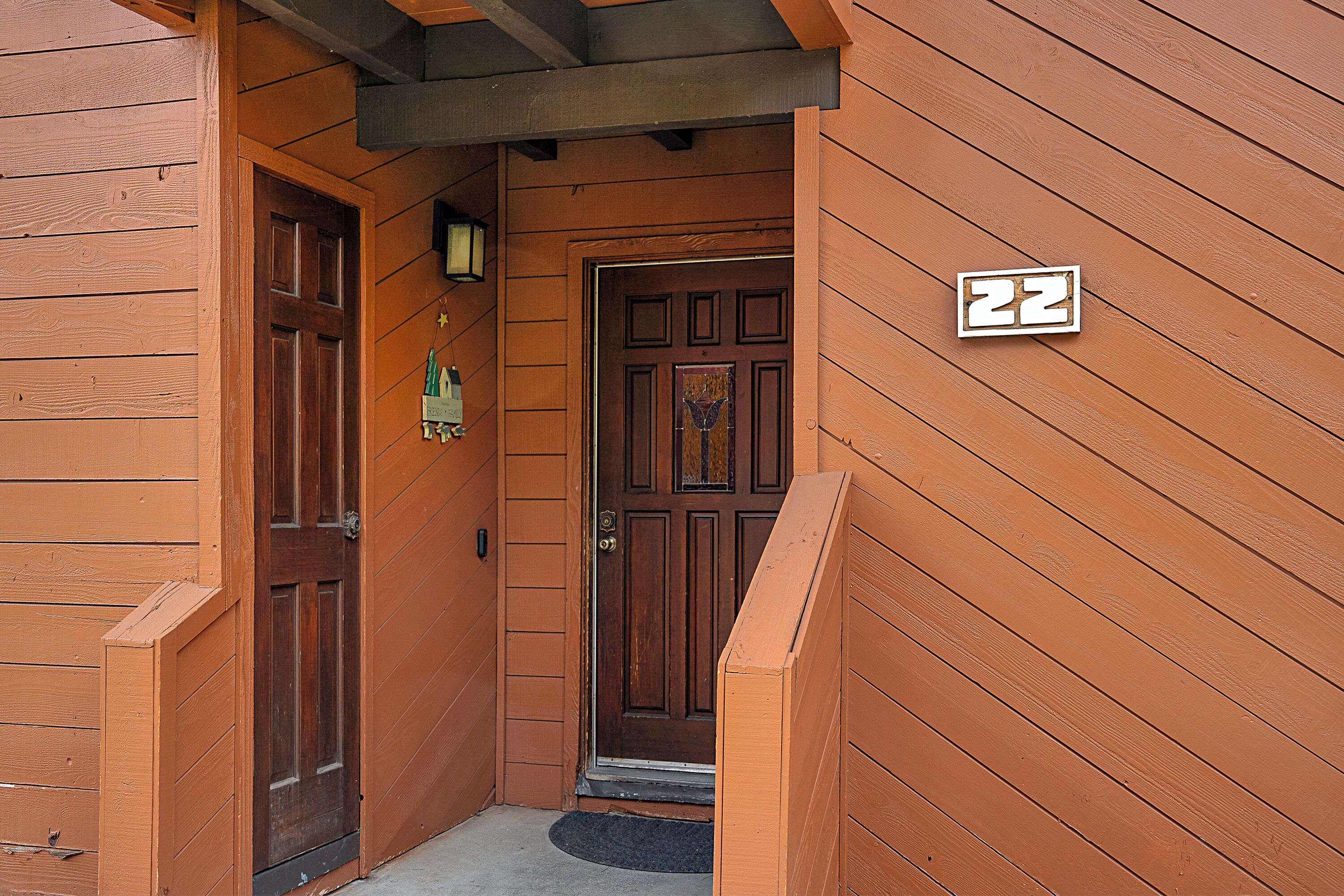 A wooden building entrance with a door, a number plaque, and a small porch area.