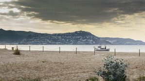 A beach with a boat on the water, a fence, and mountains in the background. - Pleasant one bedroom apartment (Empuriabrava)