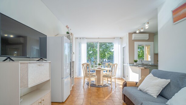 A compact living space with a kitchenette, a dining area with a table and chairs, a sofa, and a television. - Pleasant one bedroom apartment (Empuriabrava)