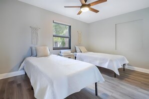 Two single beds with white bedspreads, a ceiling fan, and a large window.