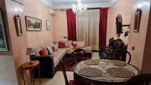 Ein Wohnzimmer mit einer Couch, einem Esstisch, Stühlen, einer Chandelieber und einem Fernseher.