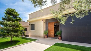 Una casa moderna de dos pisos con un césped cuidado, plantas en macetas y un cielo despejado.