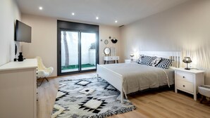 Un dormitorio con cama, mesitas de noche, televisor y ventana grande.