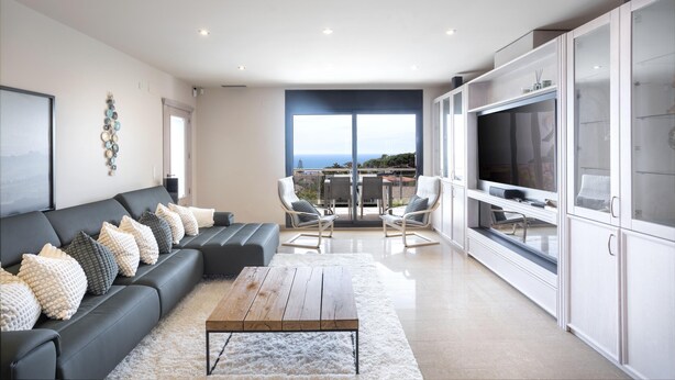 Una sala de estar moderna con un sofá negro, una mesa de centro de madera y un televisor grande. Hay un balcón con vista a la ciudad.