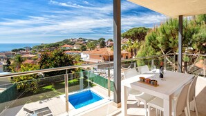 Un balcón con baranda de cristal que da a una piscina y vistas al mar y casas cercanas.