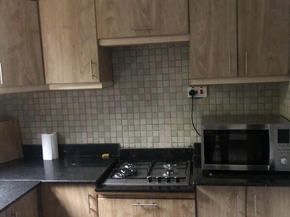 A kitchen with wooden cabinets, a tiled backsplash, a gas stove, and a microwave.