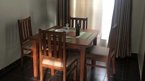 Zona pranzo con tavolo in legno e quattro sedie, una lampada da tavolo e una finestra con tende.