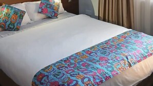 Una camera d'albergo con un letto grande, una testiera in legno, due cuscini colorati, una coperta a motivi e tende color beige.