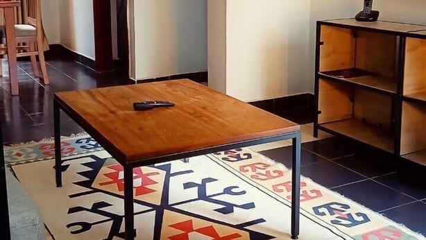 Un soggiorno con un tavolino in legno, un tappeto decorato, una TV su un mobile e una porta che dà su un'altra stanza.