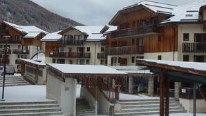 Een besneeud skiëresort met houten gebouwen, balkons en een berg op de achtergrond.