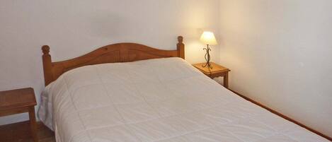 A single bed with a wooden headboard, a bedside table with a lamp, and a framed picture on the wall.