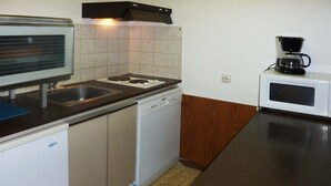 Una cocina compacta con estufa, fregadero, lavavajillas, microondas y cafetera.