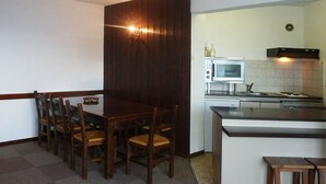Cocina compacta con comedor, que incluye una mesa y sillas de madera, un microondas y una pequeña isla con taburetes.