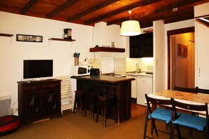 Cocina pequeña equipada con microondas, tostadora y lavamanos. Zona de comedor con mesa y sillas.