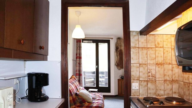 A compact kitchen with a coffee maker, a stove, and a dining area with a plaid sofa. - 32 LES Gradins lES Orres 1650 (LES ORRES 1650)