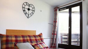 A room with a bed, a heart-shaped clock on the wall, and a window with curtains. - 32 LES Gradins lES Orres 1650 (LES ORRES 1650)