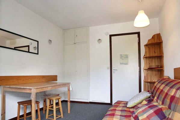 A small, cozy room with a wooden desk, two stools, a sofa with a colorful blanket, a mirror, a wardrobe, and a wooden shelf with a basket. - 32 LES Gradins lES Orres 1650 (LES ORRES 1650)