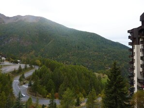 A mountainous landscape with a winding road and a multi-story building with balconies. - 32 LES Gradins lES Orres 1650 (LES ORRES 1650)