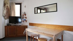 A room with a wooden table, two chairs, a television on a wooden cabinet, a mirror on the wall, and a fur coat hanging on the wall. - 32 LES Gradins lES Orres 1650 (LES ORRES 1650)